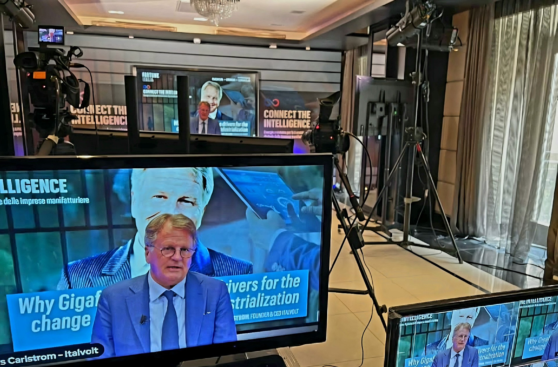 Lars Carlstrom on a studio monitor during a television interview, seen from behind the broadcast cameras