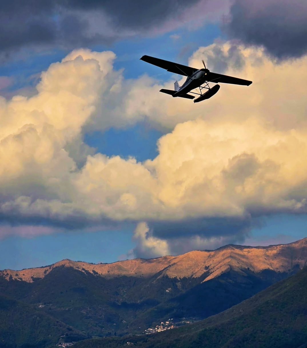 Seaplane flying above mountains beneath sunlit clouds