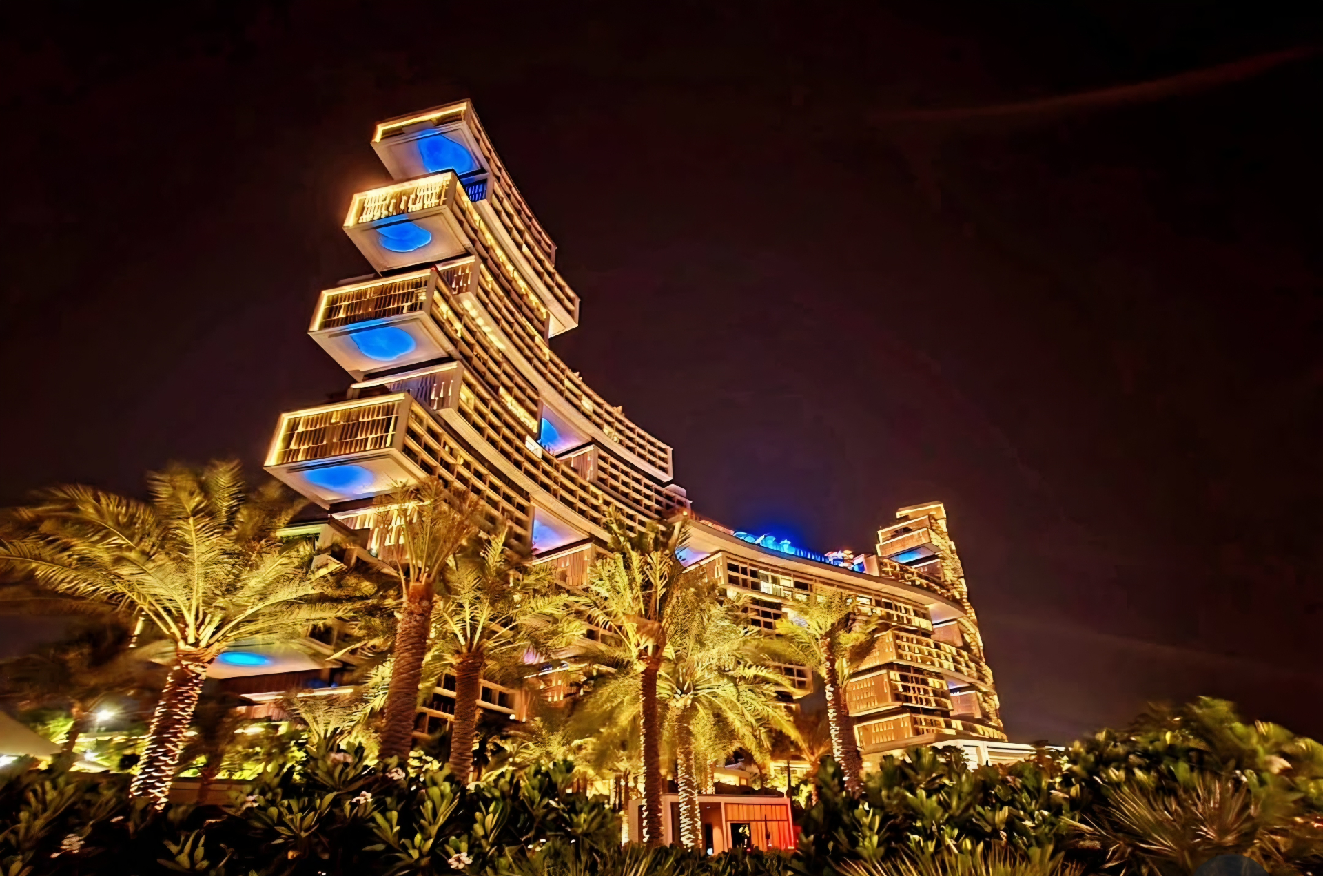 Illuminated building with projecting terraces and palms at night