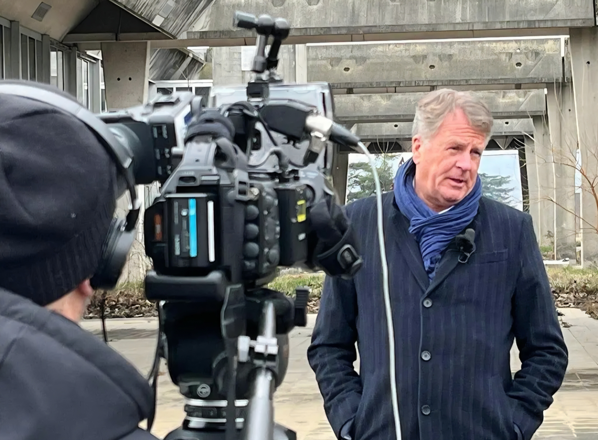 Lars Carlstrom being filmed for an interview outside a concrete building