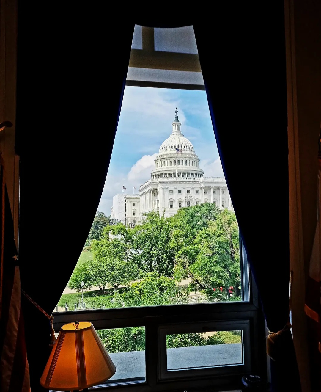 United States Capitol viewed through a window framed by dark curtains