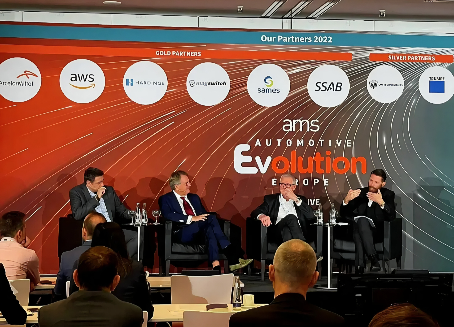 Four speakers on stage at the Automotive Evolution Europe panel beneath a 2022 partner banner