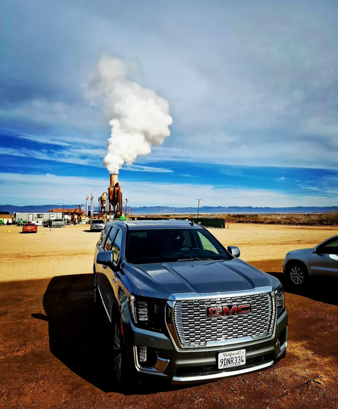 GMC SUV parked beside an industrial site with steam rising from a tower