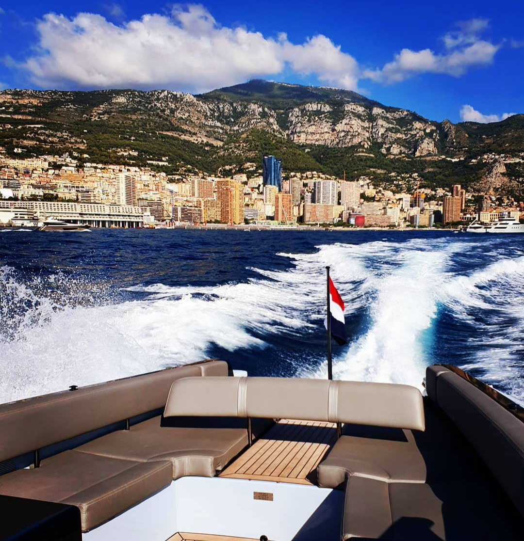 Monaco’s waterfront and mountains seen from a boat leaving a white wake