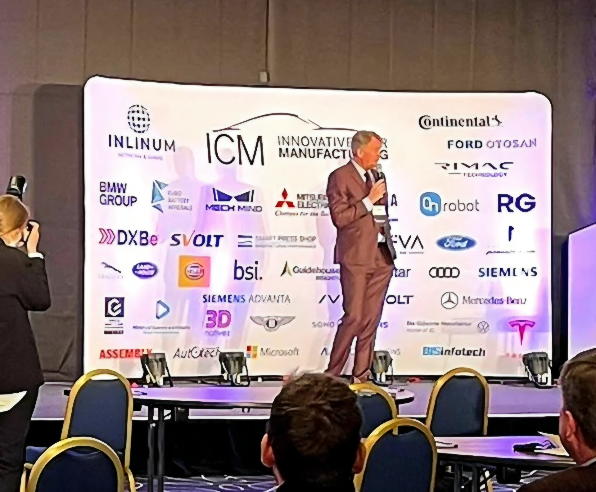 Lars Carlstrom speaking on stage in front of an Innovative Manufacturing sponsor backdrop